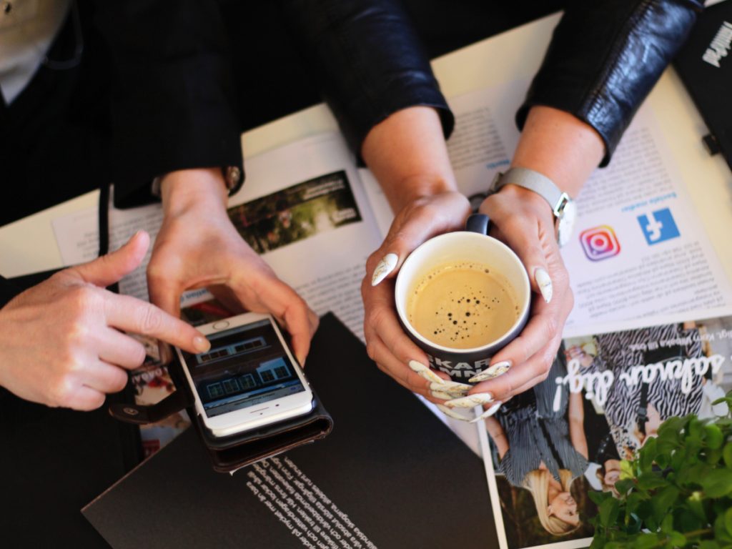 Närbild på händer med mobiltelefon och kaffe.
